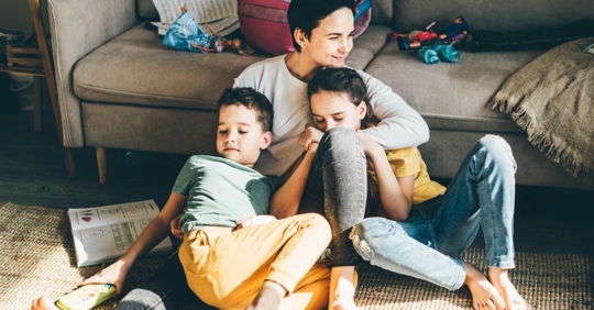 Mother hugging her son and daughter while sitting on the floor of their living room