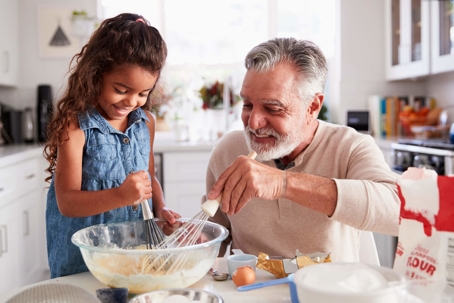 Granddad with granddaughter whisking batter in bowl