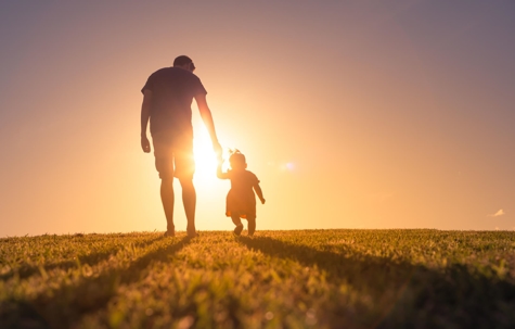 Father and daughter walking in field at sunset