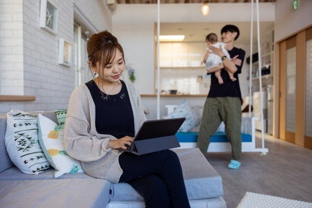 mother typing on tablet with father and baby in the background