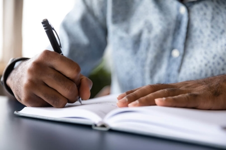 Man writing in open notebook on table.