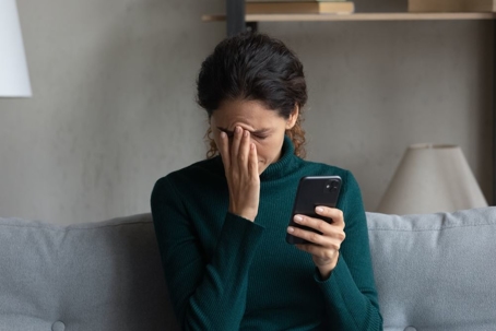Woman with hand on face holding cell phone.